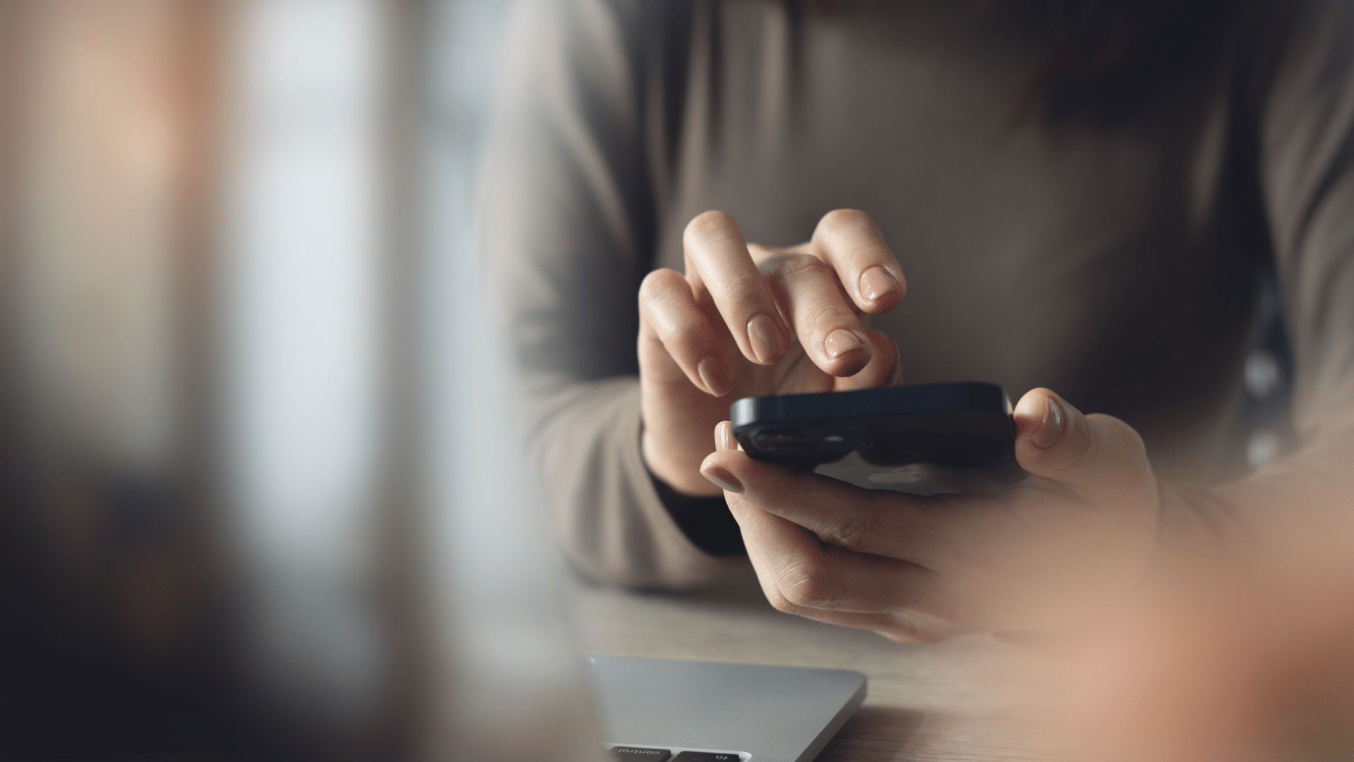 Business woman using mobile phone with laptop computer on office table