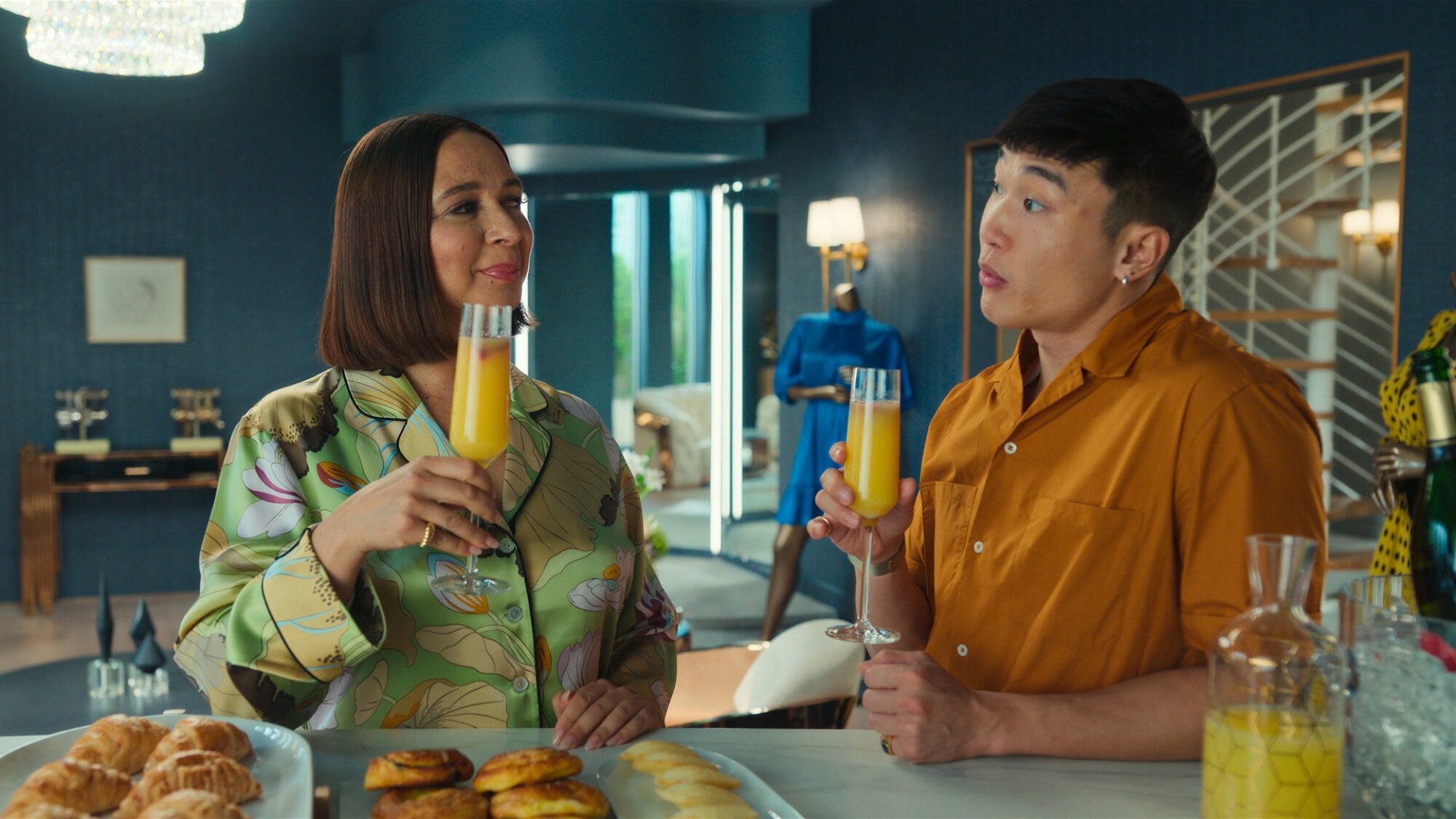 A woman and a man cheer mimosas from a breakfast bar.