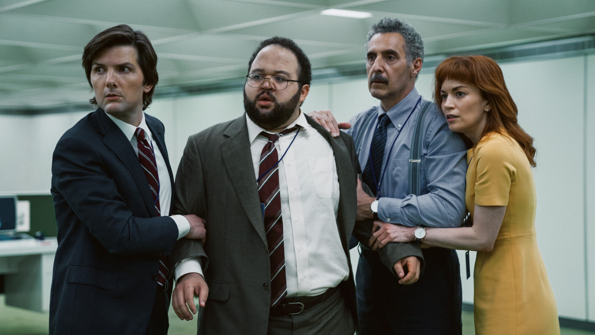 Four office workers in the TV show "Severance" look concerned, played by Adam Scott, Britt Lower, Zach Cherry, and John Turturro.