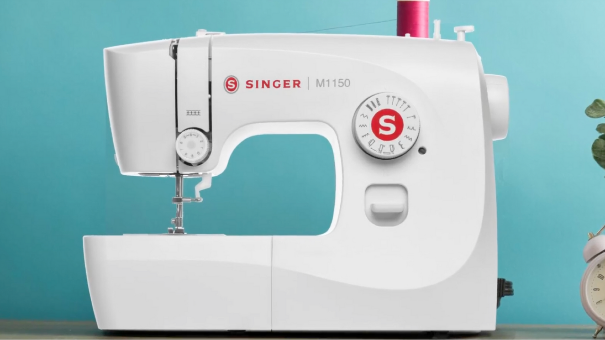 white singer sewing machine with pink thread against a turquoise background