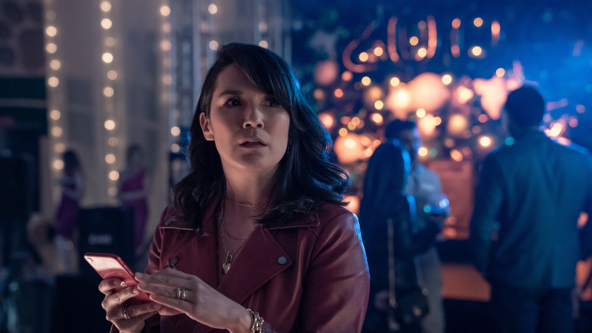 A woman looks concerned at a party on her phone.