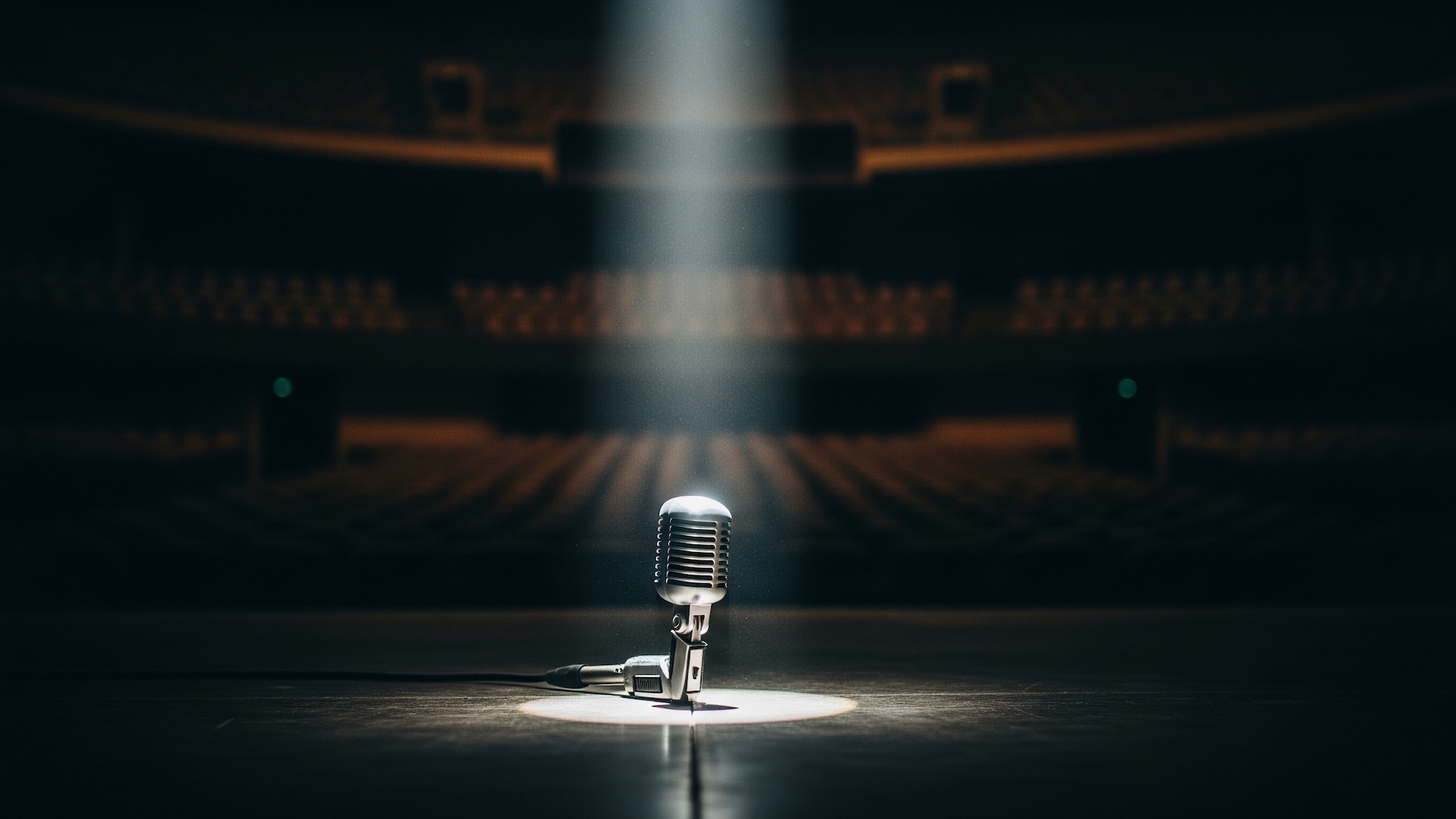 A single microphone on a dimly lit stage, spotlight cutting through shadows.